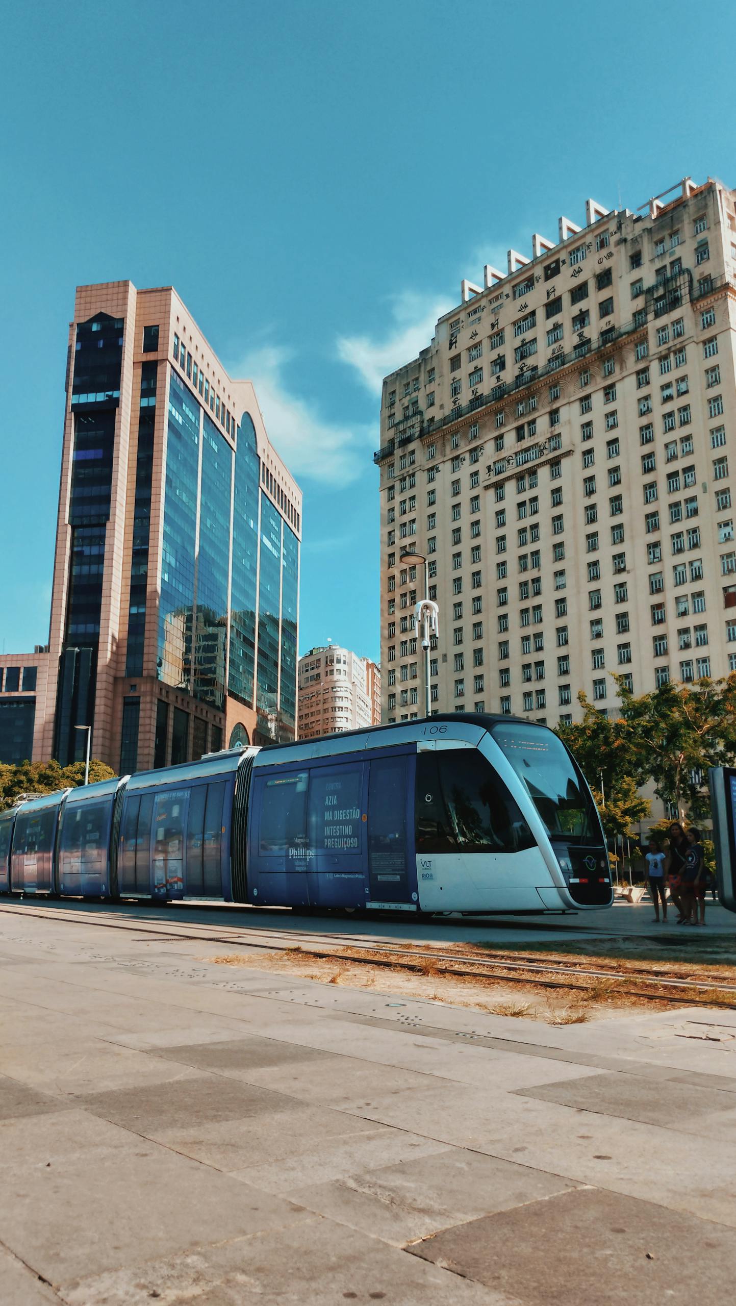 A modern tram passes through the bustling urban center of Rio de Janeiro, Brazil, surrounded by skyscrapers.