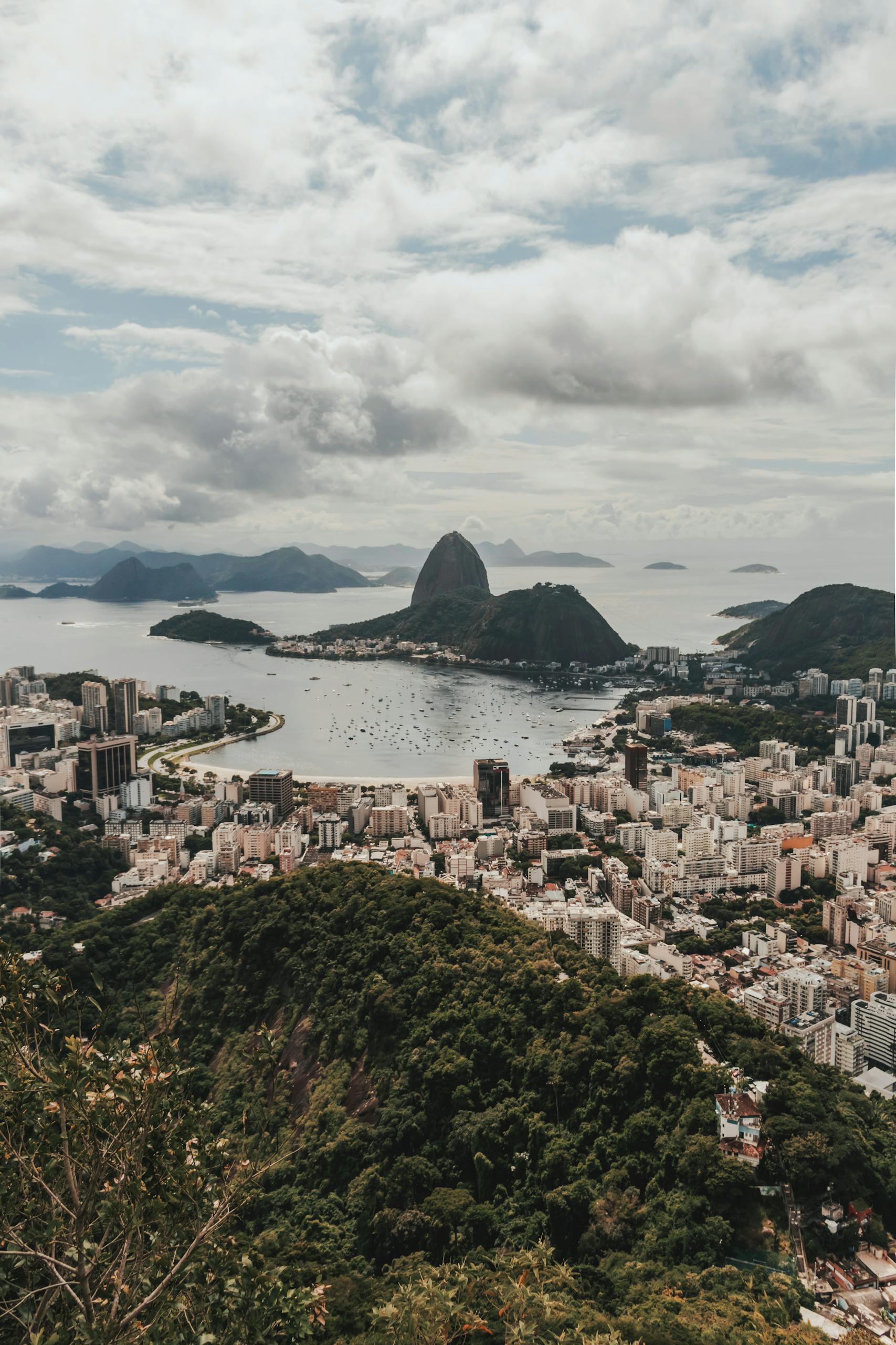 Stunning aerial view of Rio de Janeiro's cityscape with Sugarloaf Mountain in Brazil under a cloudy sky.